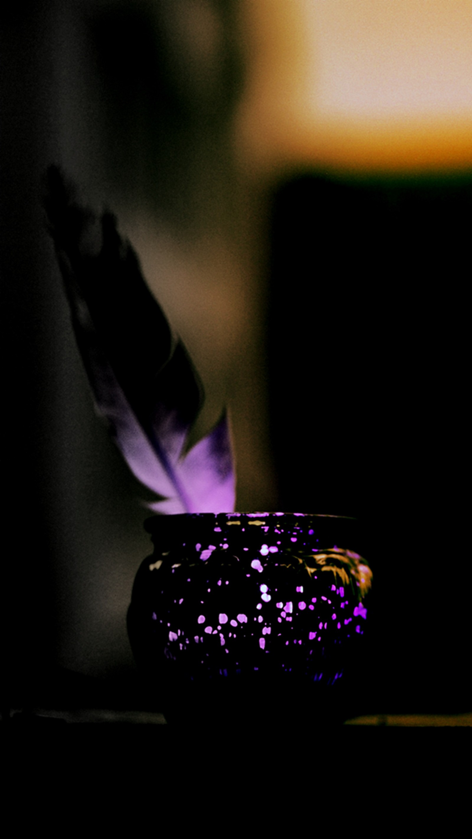 Une bougie en verre violette avec une plume dessus, posée sur une table (plume, pétillant)