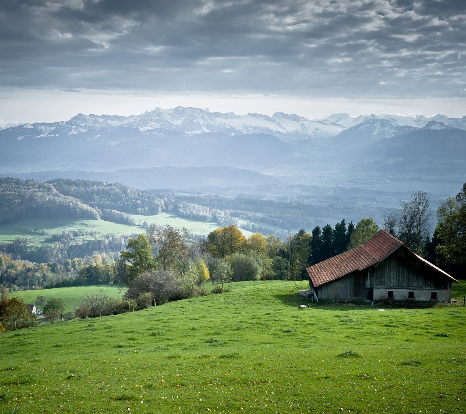 Montanhas ao longe com um celeiro em primeiro plano (grama, verde, casa, paisagem, montanhas)