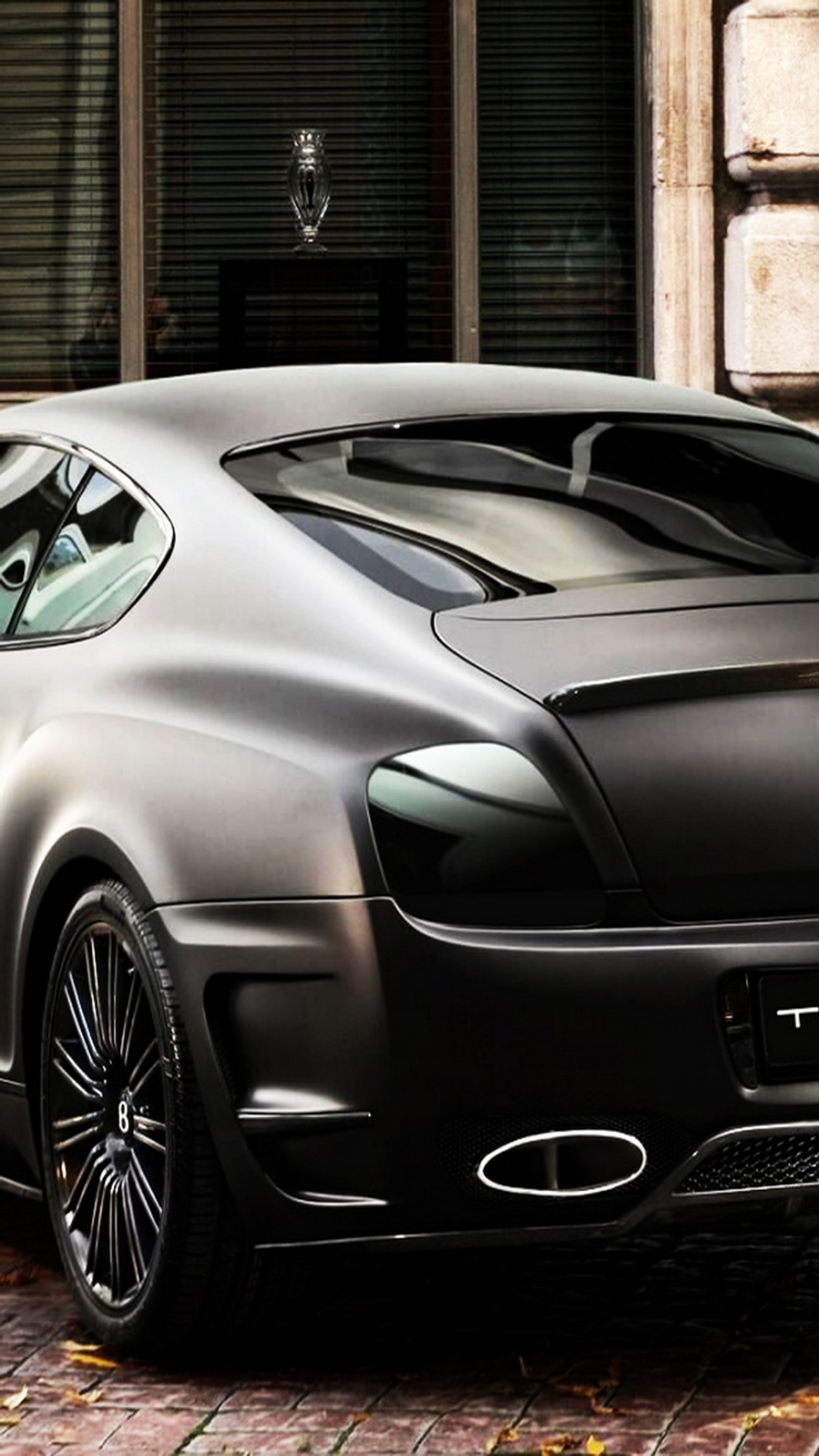 Un coche deportivo negro estacionado en una acera de ladrillos frente a un edificio (bentley, bentley continental, negro, continental)