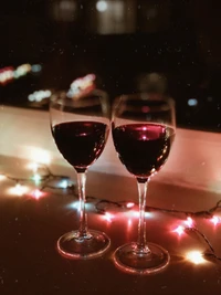 Dois elegantes copos de vinho cheios de vinho tinto, iluminados por luzes festivas coloridas.