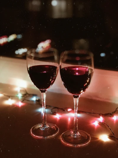 Deux élégants verres à vin remplis de vin rouge, illuminés par des lumières festives colorées.