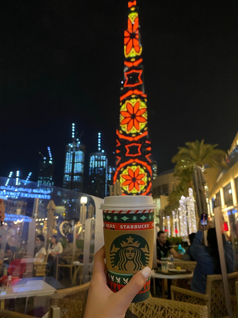 Кто-то держит чашку starbucks перед рождественской елкой (дубай, dubai, burj khalifa, ночь, башня)