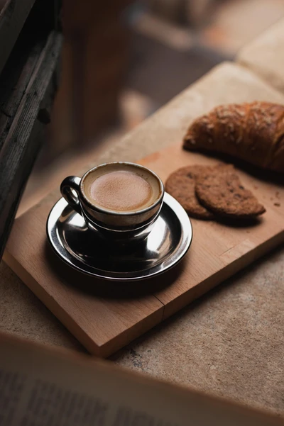 Elegant coffee cup with espresso, cookies, and a croissant on a wooden platter.