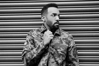 Monochrome portrait of a gentleman in a camo jacket, exuding confidence and style against a patterned backdrop.