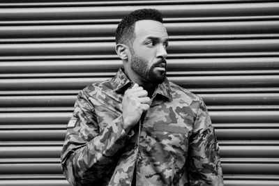 Monochrome portrait of a gentleman in a camo jacket, exuding confidence and style against a patterned backdrop.