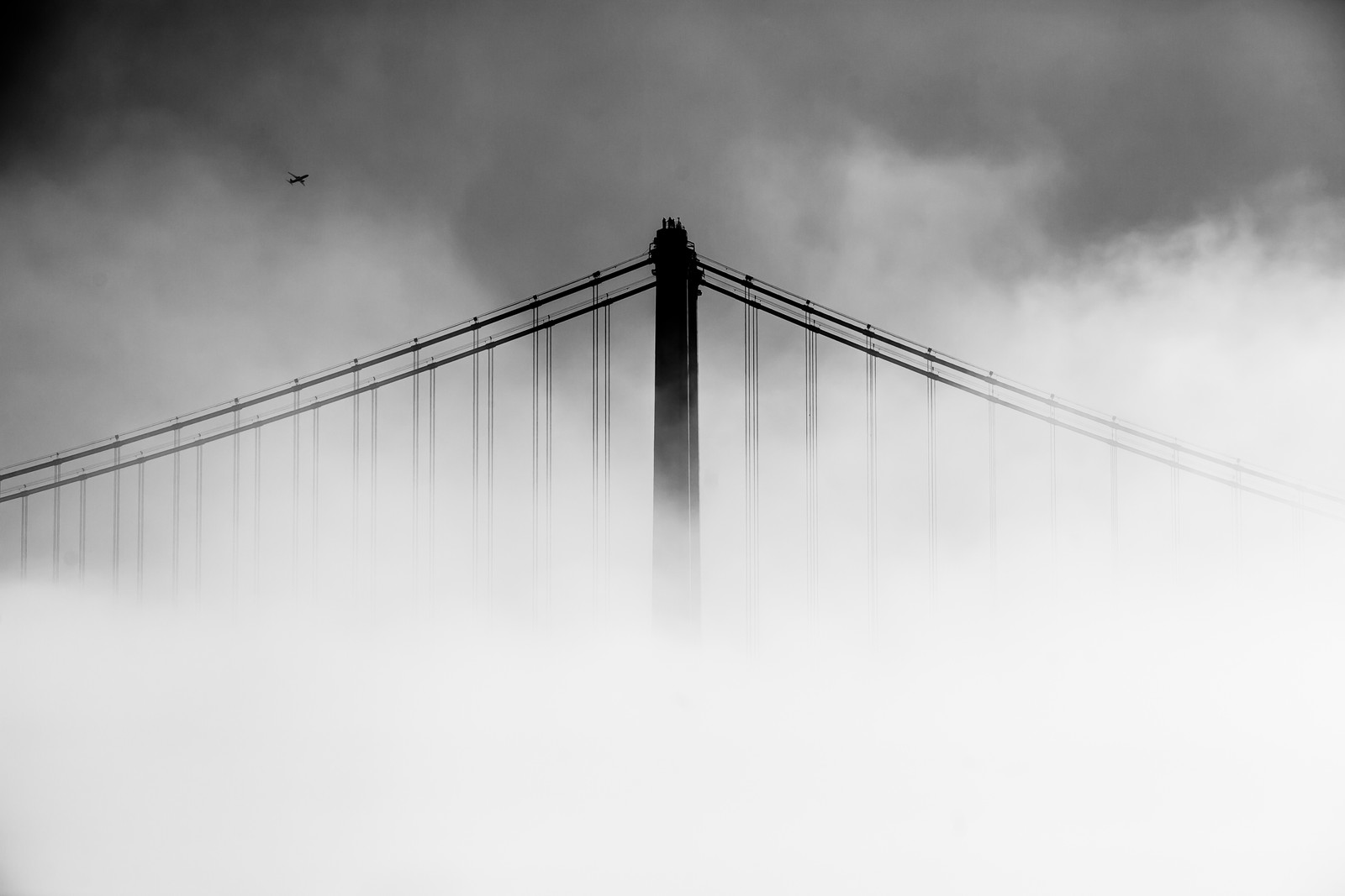 Vue d'un pont dans le brouillard avec un avion passant (blanc, eau, noir, pont, journée)