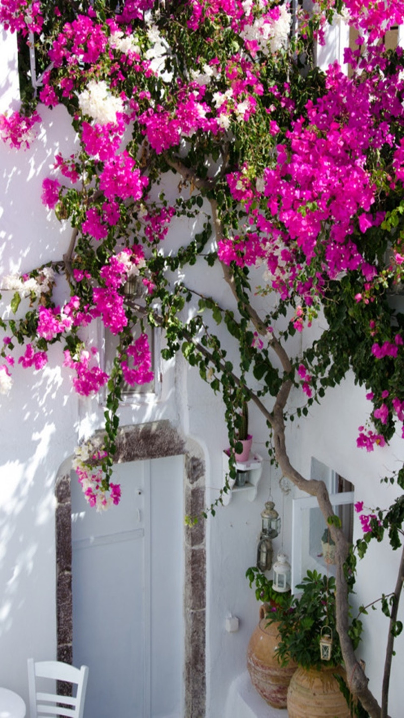 Hay una mesa blanca y sillas afuera de un edificio (flores, primavera)