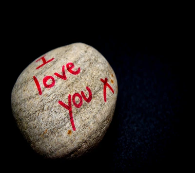 A rock with the words "I love you" painted in red on its surface, set against a black background.