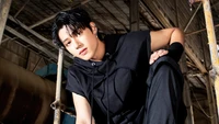 Wooyoung do ATEEZ posando confiantemente em um ambiente industrial, exibindo um traje preto estiloso.