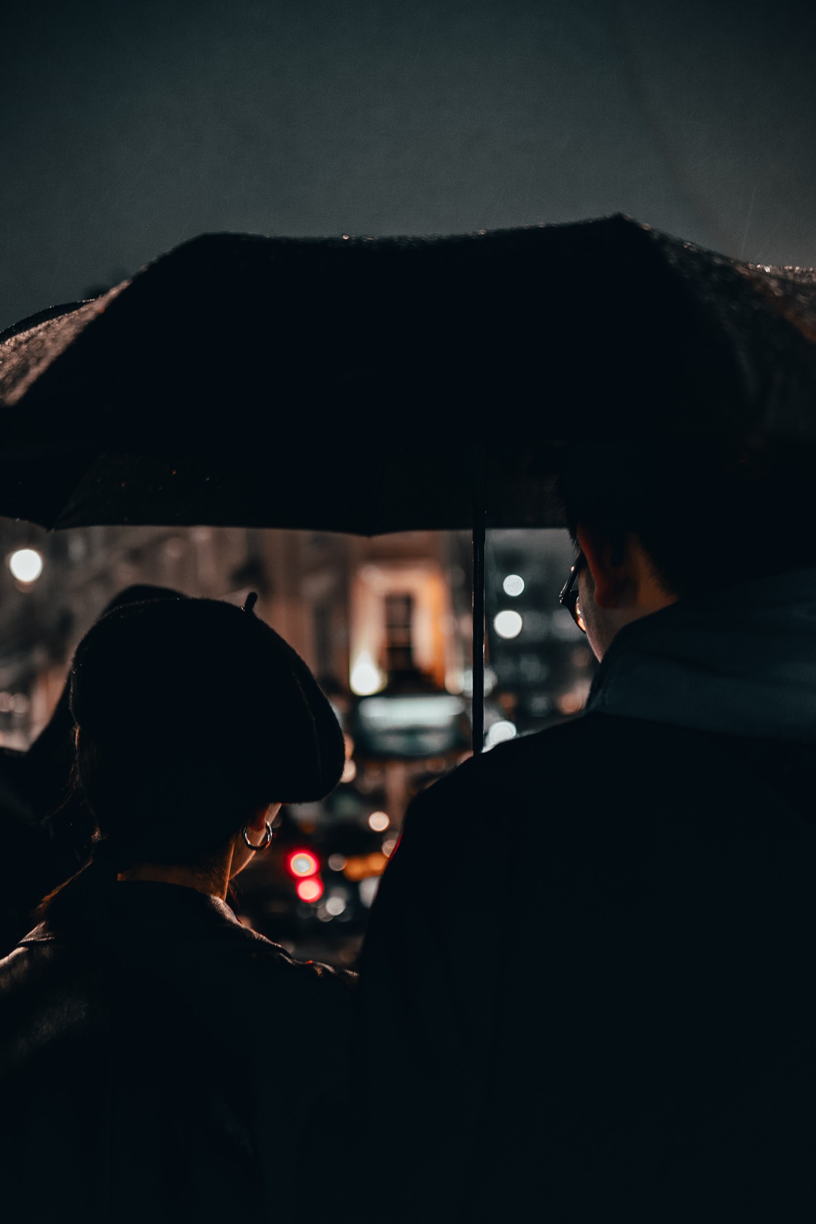 Deux personnes debout sous un parapluie sous la pluie (lumière, réflexion, éclairage automobile, obscurité, nuit)