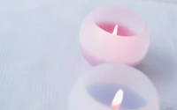 Velas rosa e roxas brilhando suavemente piscam gentilmente, lançando uma luz serena contra um fundo texturizado.