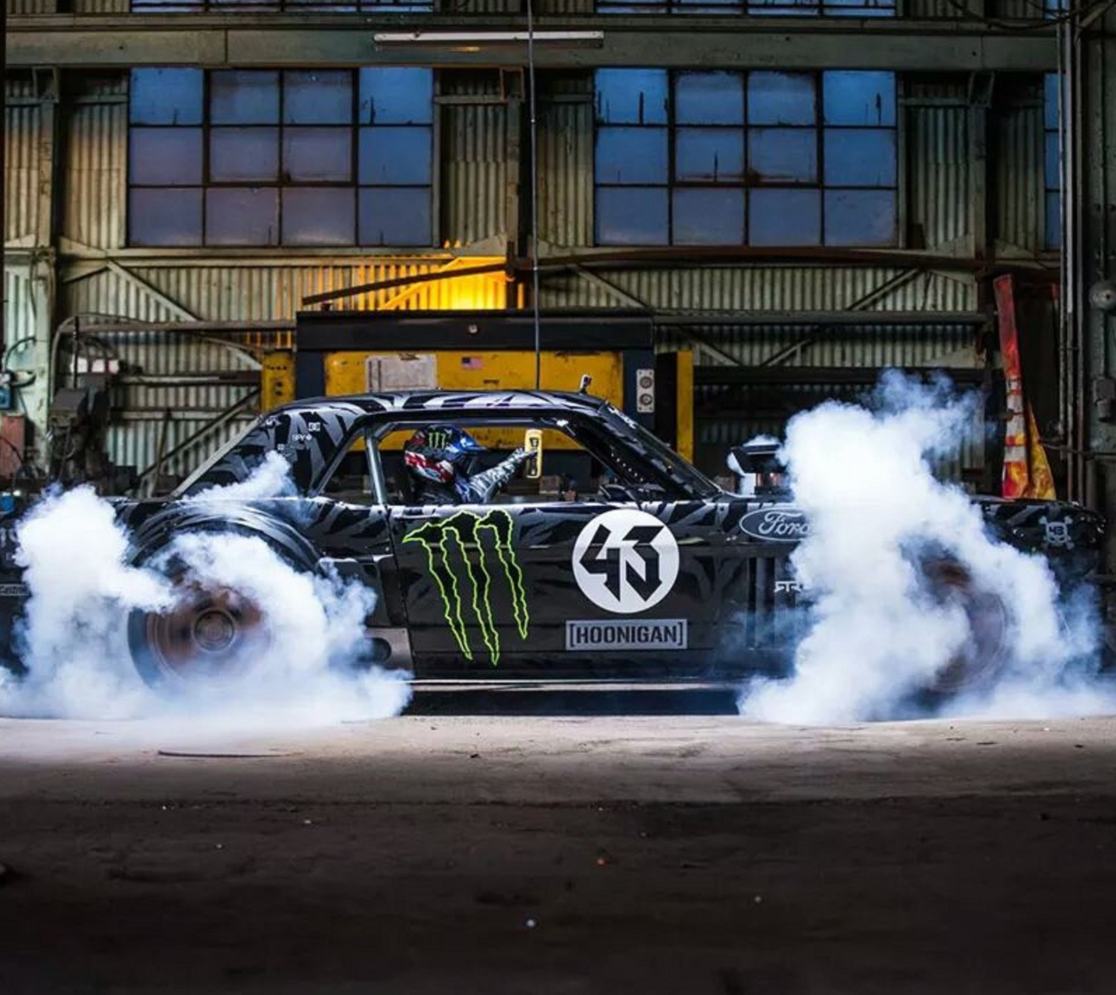 Un primer plano de un coche con humo saliendo de él (ford mustang, gymkhana siete, hoonigan, ken block)