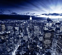 A breathtaking nighttime skyline of a vibrant city, illuminated by countless lights against a deep blue sky, featuring a prominent skyscraper.