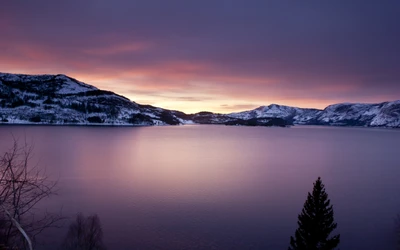 Dawn's tranquil reflection over a snow-capped lake surrounded by mountains.