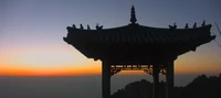 Silhouette d'un pavillon chinois traditionnel contre un ciel de coucher de soleil vibrant, mettant en valeur son architecture historique en tant que point de repère dans un paysage serein.