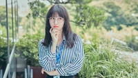 Hirai Momo com camisa listrada e óculos contra um fundo exuberante