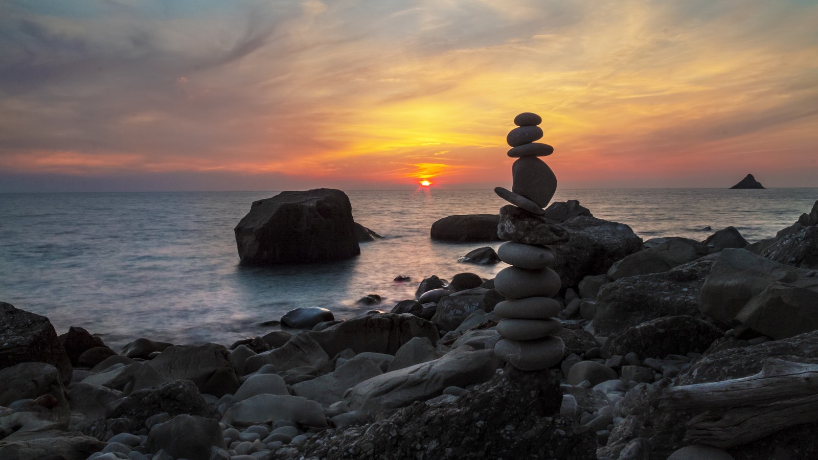 Un gros plan d'un tas de pierres sur une plage rocheuse au coucher du soleil (mer, la côte, nuage, nature, eau)