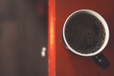 Vista de cima de uma caneca de café preta sobre uma superfície vermelha vibrante