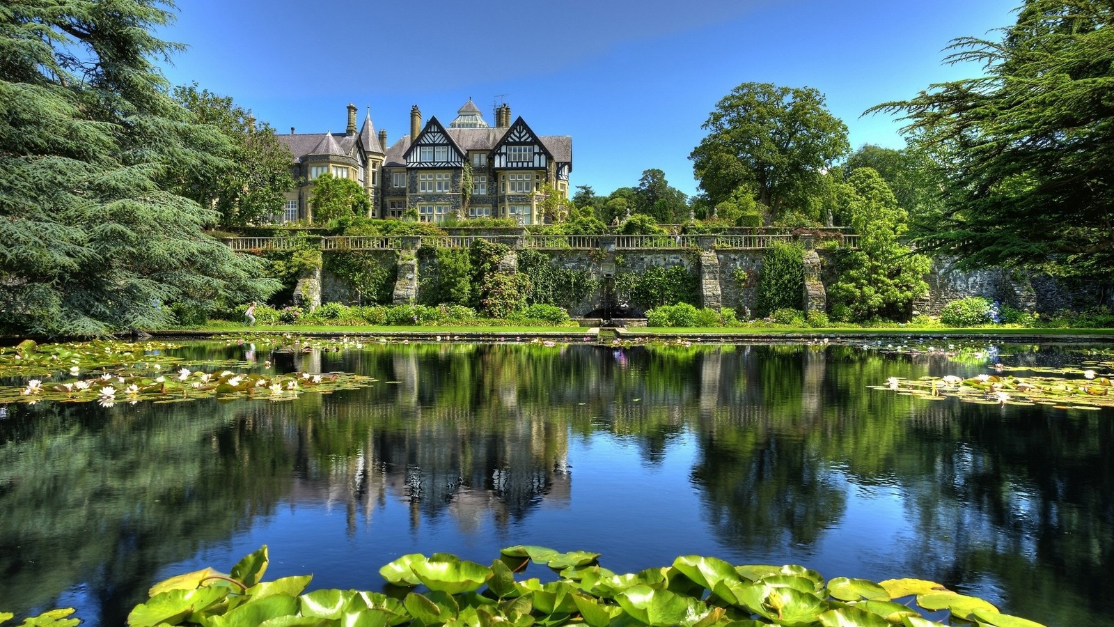 Une grande maison située sur un champ verdoyant à côté d'un lac (jardin, nature, réflexion, bien immobilier, voie navigable)