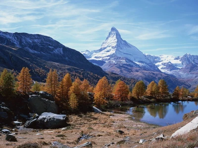 Majestic mountain peak reflecting in a tranquil lake, surrounded by autumn foliage and rugged wilderness.