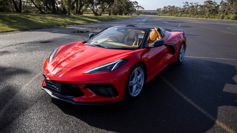 Красный спортивный автомобиль едет по дороге с деревьями на фоне (chevrolet corvette stingray convertible, 2024, спортивные автомобили, 5k, 8k)