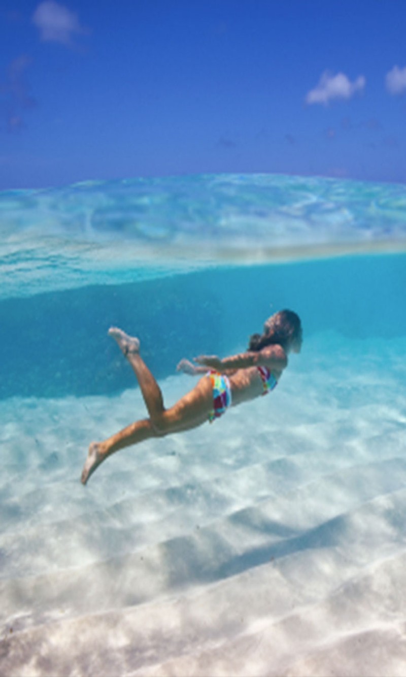 Una mujer está nadando en el océano con una tabla de surf (debajo, agua)