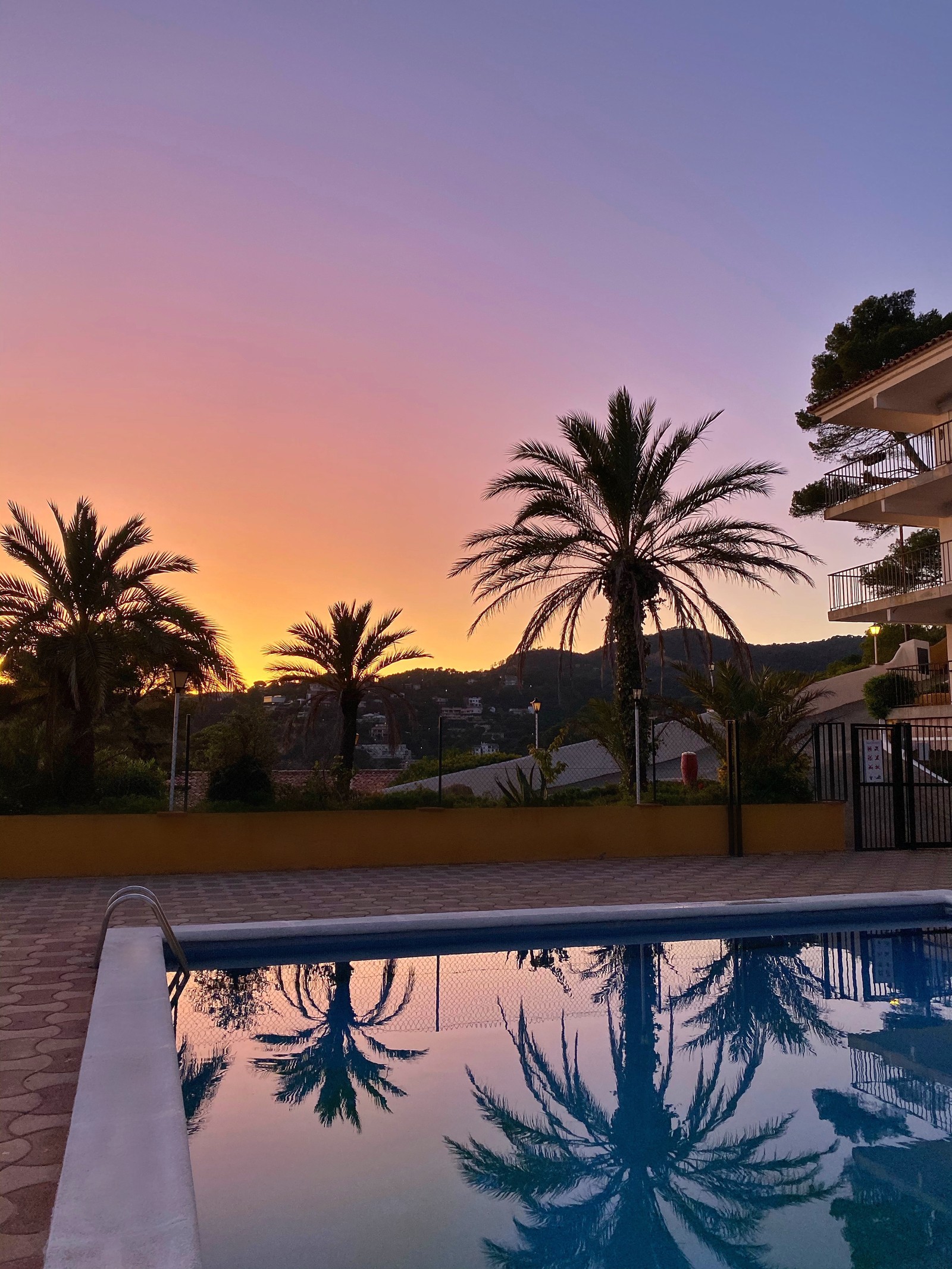 Existe uma piscina no meio de um pátio com vista para as montanhas. (reflexo, piscina, palmeiras, água, imóveis)