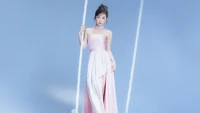 Irene from Red Velvet posing gracefully on a swing in a pastel pink gown against a soft blue background.