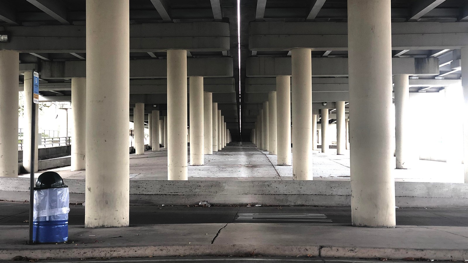 Hay un bote de basura azul debajo de un puente (columna, sombra, gris, estilo, blanco y negro)