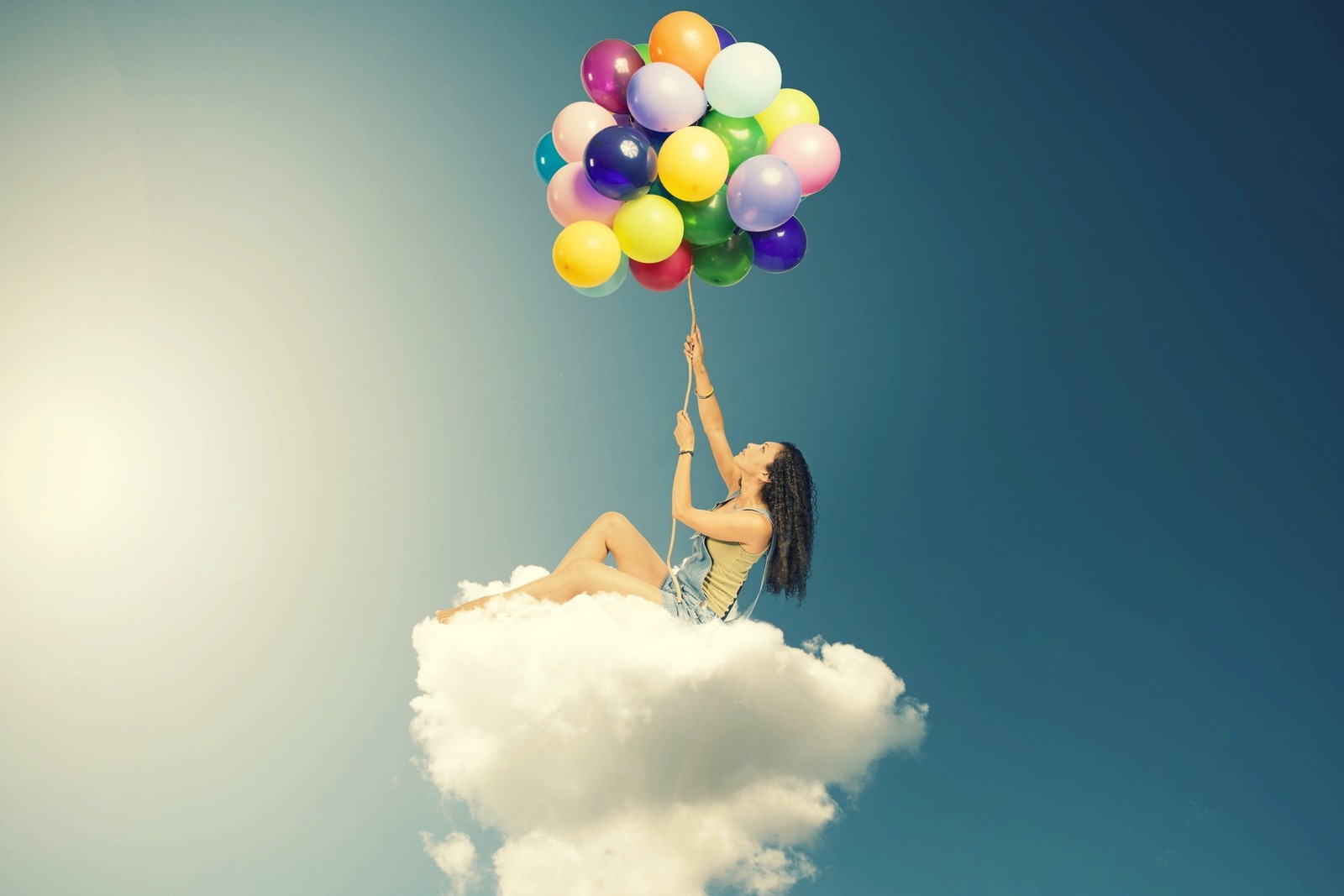 Une femme assise sur un nuage tenant un bouquet de ballons (ballon, nuage, fournitures de fête, amusement, montgolfière)