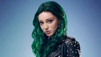 Emma Dumont com cabelos verdes marcantes, exalando confiança em uma jaqueta de couro com tachas contra um fundo vibrante.