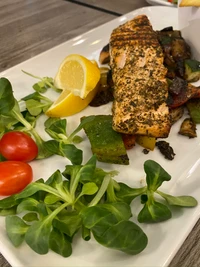 Grilled salmon with fresh greens, cherry tomatoes, and citrus garnish.