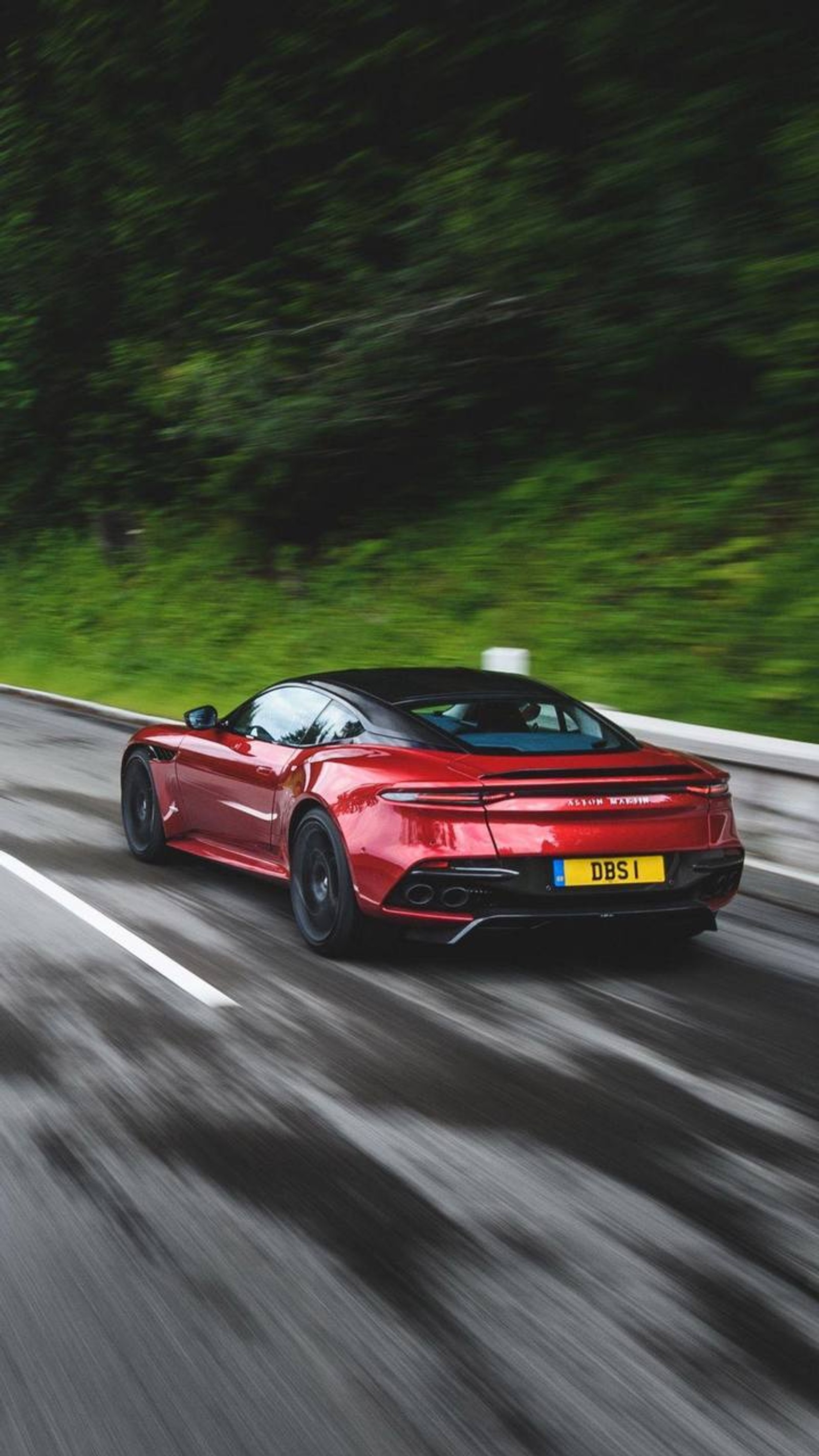 Arafed red sports car driving on a wet road with trees in the background (aston martin dbs, aston martin, cars, sports car, aston martin db11)