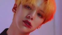 Minhyuk von Monsta X strahlt Charisma mit seinen auffälligen orangefarbenen Haaren und seinem intensiven Blick aus und verkörpert das Wesen von K-pop.