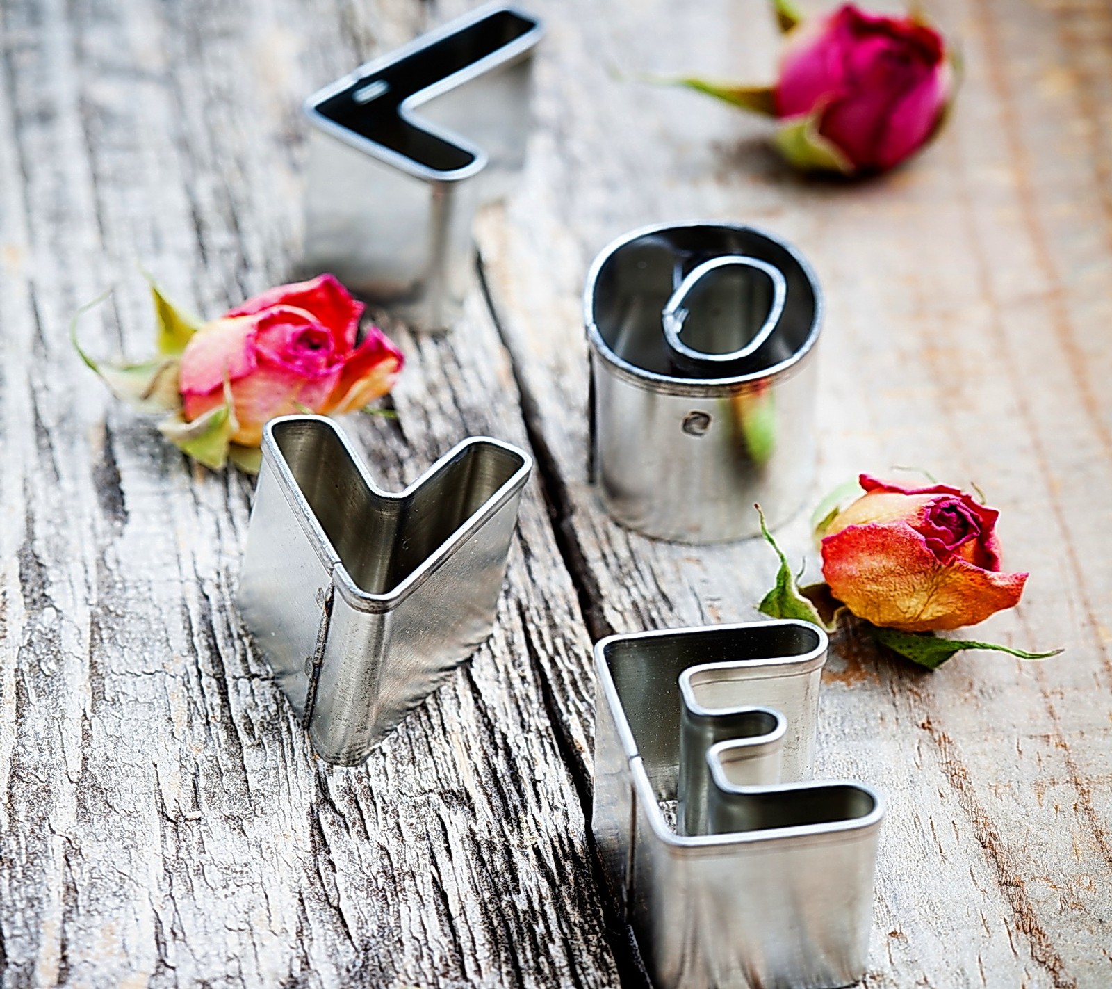 Il y a trois emporte-pièces en métal avec une rose sur une table en bois (bourgeon, amour, métallique, rose, bois)