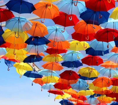 Des parapluies colorés suspendus contre un ciel bleu clair.