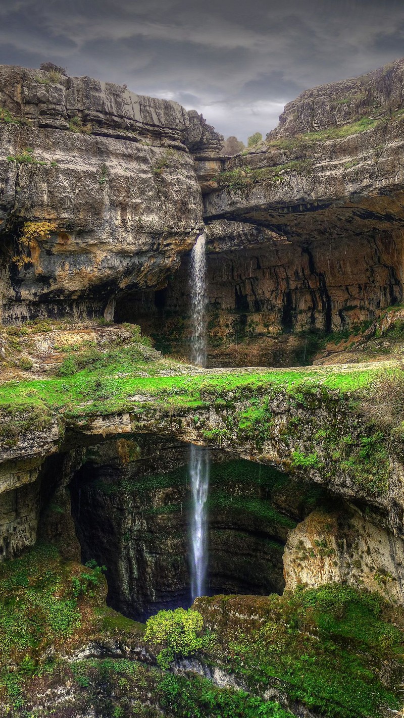 A view of a waterfall in a canyon with a green field below (baatara gorge, lebanon, tannourine, waterfall)