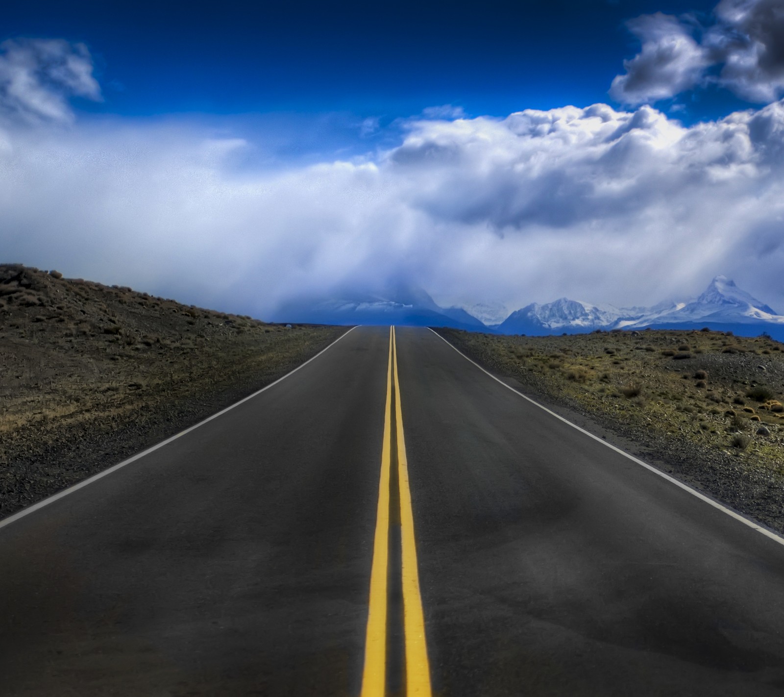 Une route panoramique avec des lignes jaunes menant à des montagnes et des nuages (art, beau, nuages, couleurs, paysage)