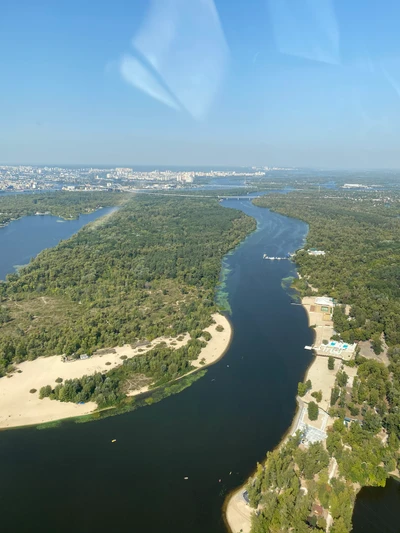 Вид с воздуха на извивающийся водный путь, окруженный зелеными насаждениями и песчаными пляжами.