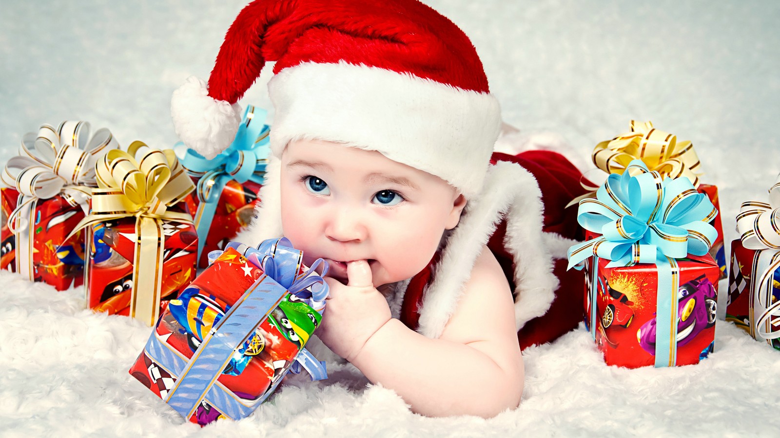 Bébé dans un chapeau de noël allongé sur la neige avec des cadeaux (père noël, nourrisson, noël, enfant, jeune enfant)