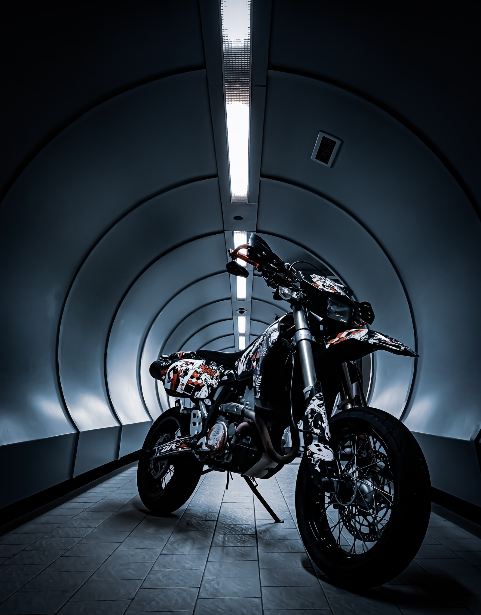 There is a motorcycle that is parked in a tunnel (motorcycle, cars, suzuki, sticker, tire)