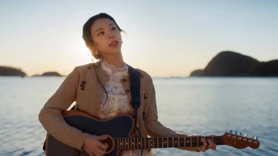 Chaeyoung performing with a guitar against a scenic sunset backdrop by the water.