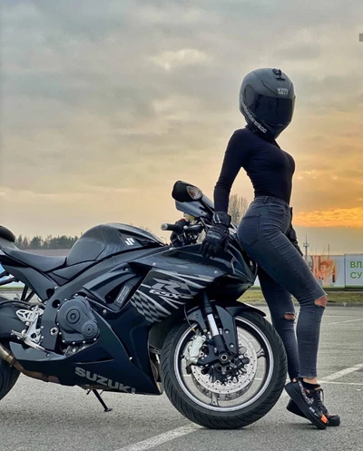 Femme motarde élégante posant avec une moto noire au coucher du soleil