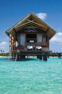 Stilted overwater villa with a thatched roof, surrounded by clear turquoise waters and a serene tropical landscape.