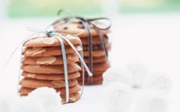 Biscoitos de amêndoa empilhados e cookies com gotas de chocolate, elegantemente amarrados com fitas, cercados por confeitos brancos.