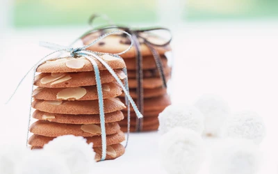 Stacked almond biscuits and chocolate chip cookies, elegantly tied with ribbons, surrounded by white confections.