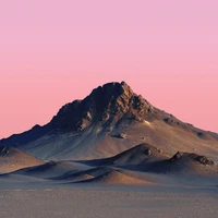 Majestic mountain peak at sunset against a pink sky, framed by desert sands.