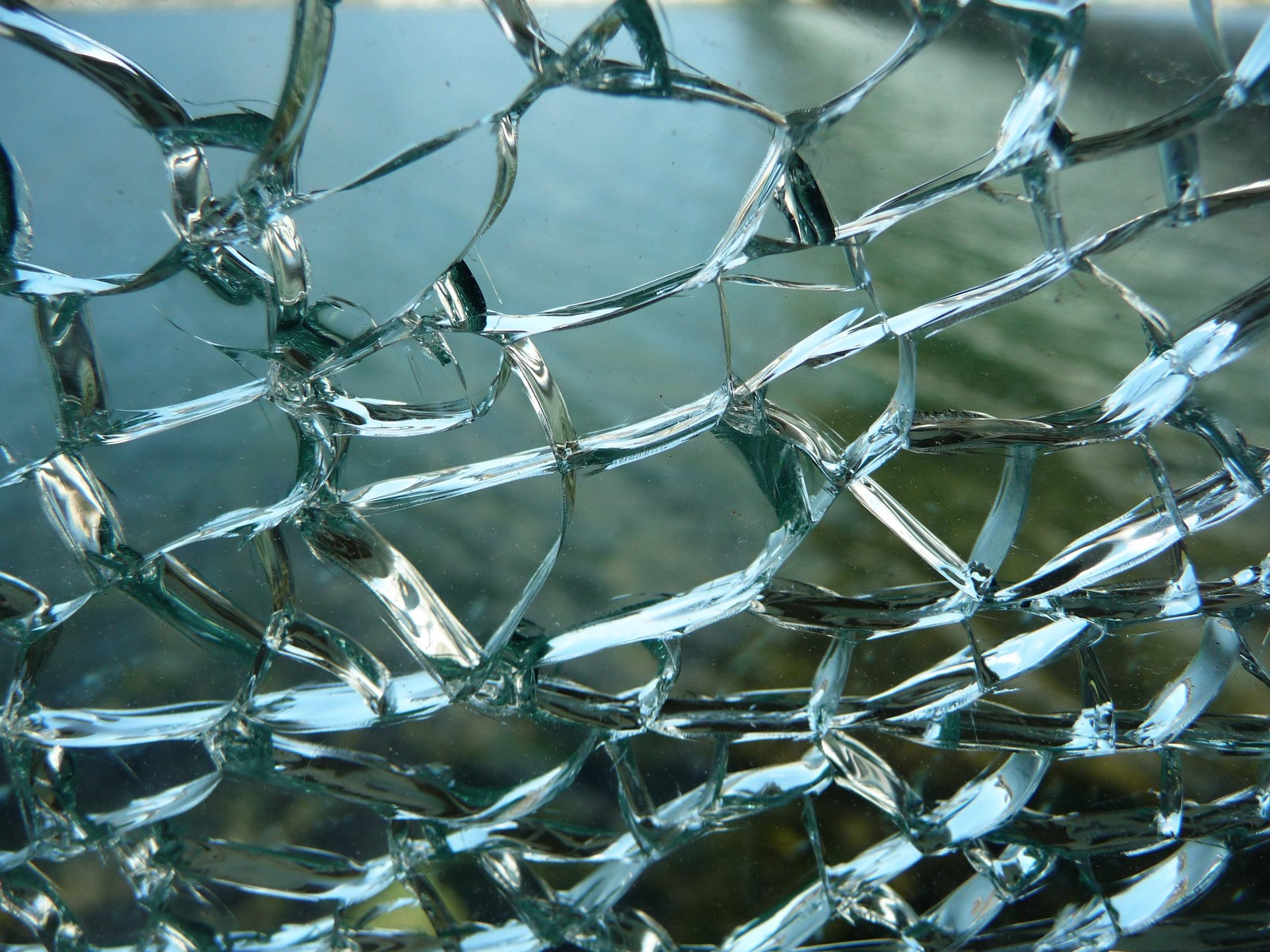 A close up of a broken glass window with a view of a body of water (glass, texture, water, wire fencing, metal)