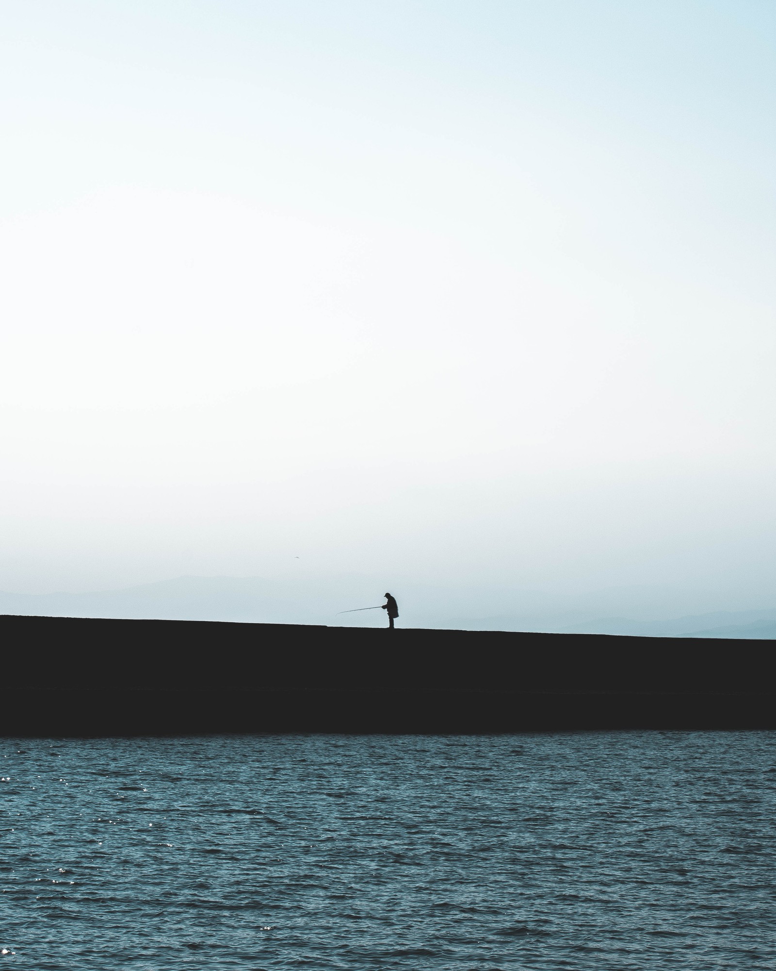 Une personne se tient sur un mur près de l'eau (horizon, eau, mer, océan, calme)