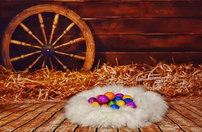 Bunte Ostereier, die in einem flauschigen weißen Nest liegen, vor einem rustikalen Holz-Hintergrund mit einem Wagenrad und Stroh.